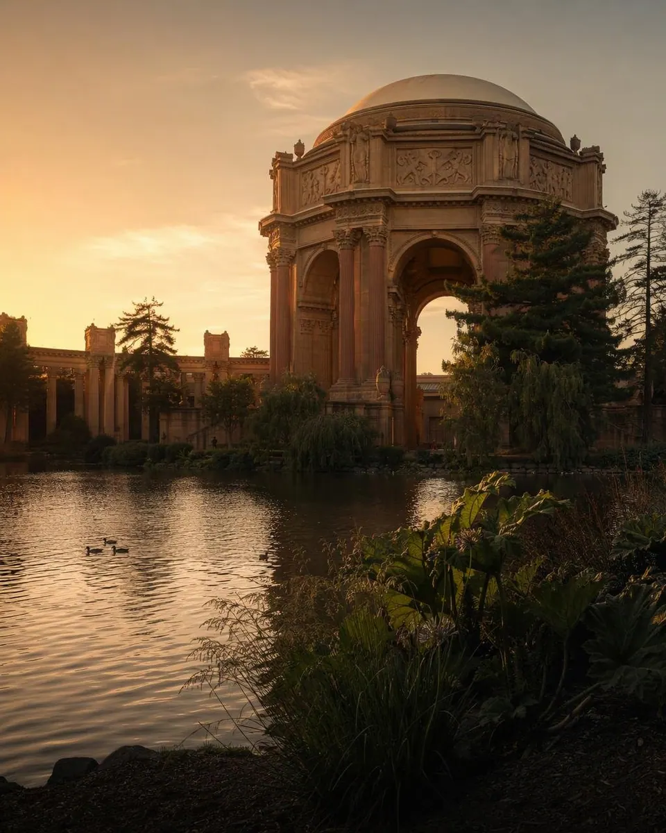 The Palace of Fine Arts rotunda and colonnade glow in golden sunset light beside the lagoon, with ducks on the water and leaves in the foreground.